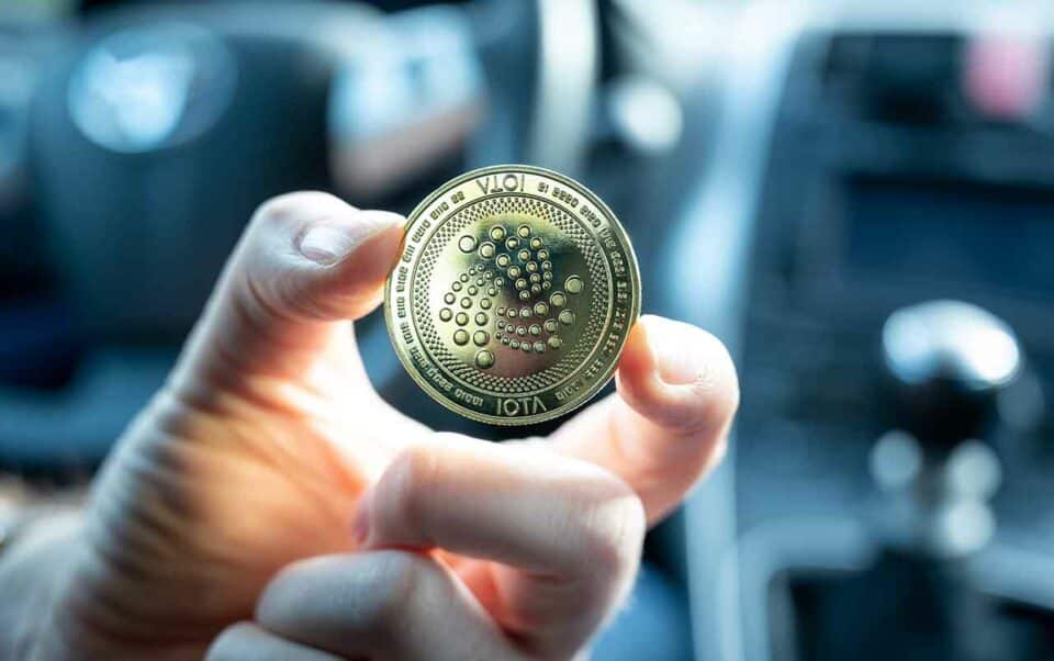 Eine Hand hält eine IOTA Münze in einem Auto